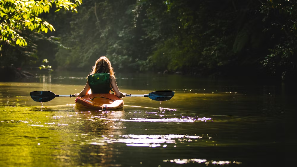 A woman is kayaking on a stream