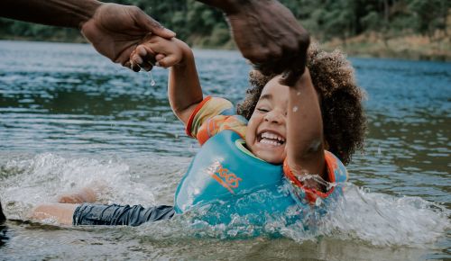 A child playing in water with parent and life jacket